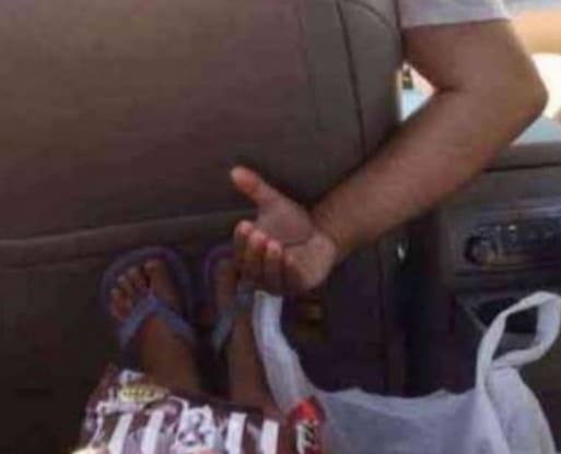 A man extending his right hand at the backseat of his car to an unknown child that has a pack of M&Ms.